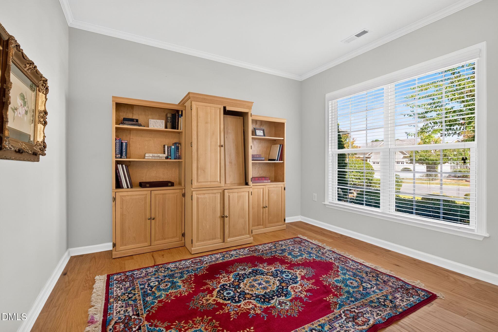 Home office with built-in wood bookcases, hardwood floors, and a large patterned rug.