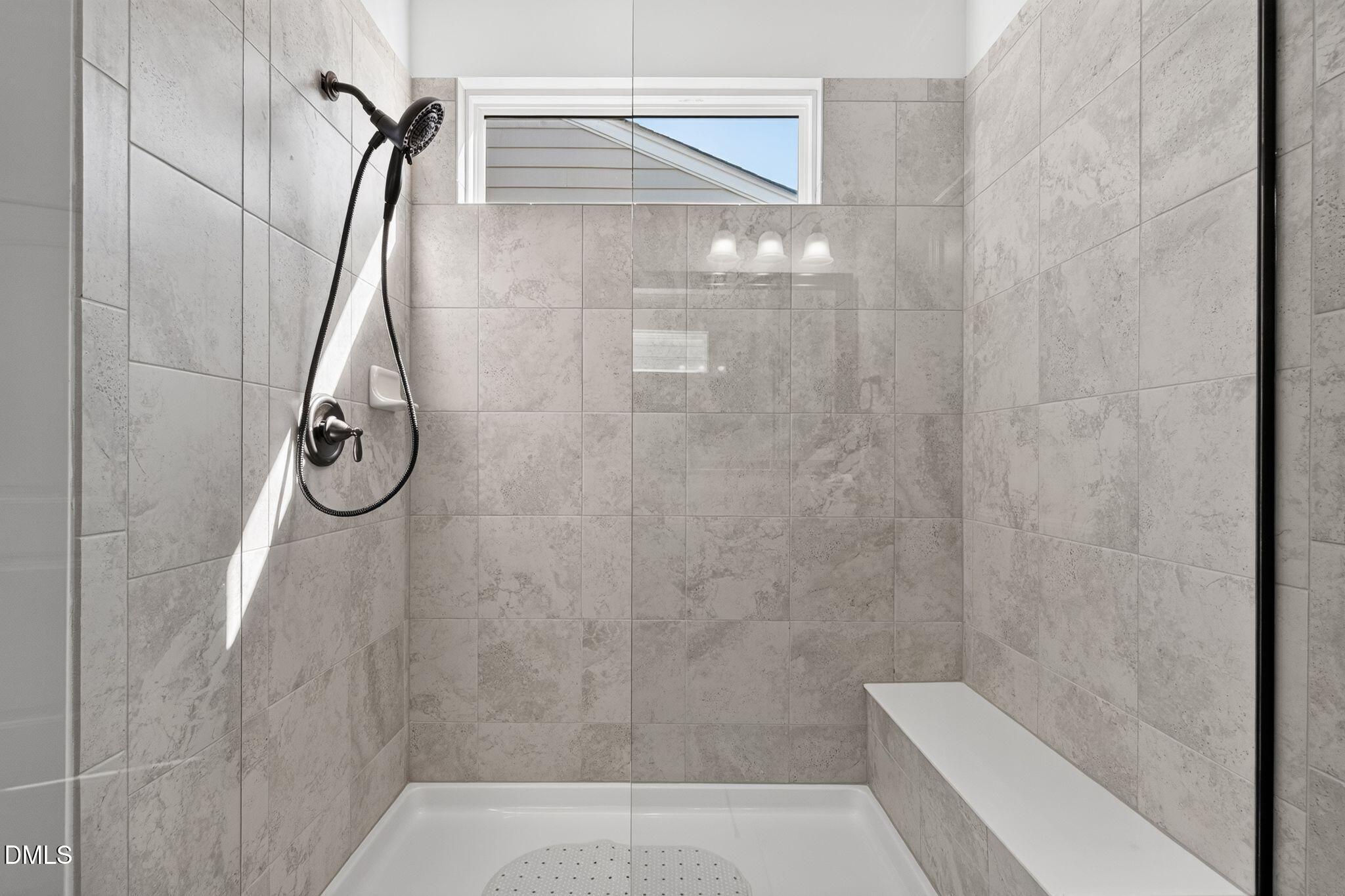 Walk-in shower with gray stone-look tile, glass enclosure, dark showerhead, and built-in bench.