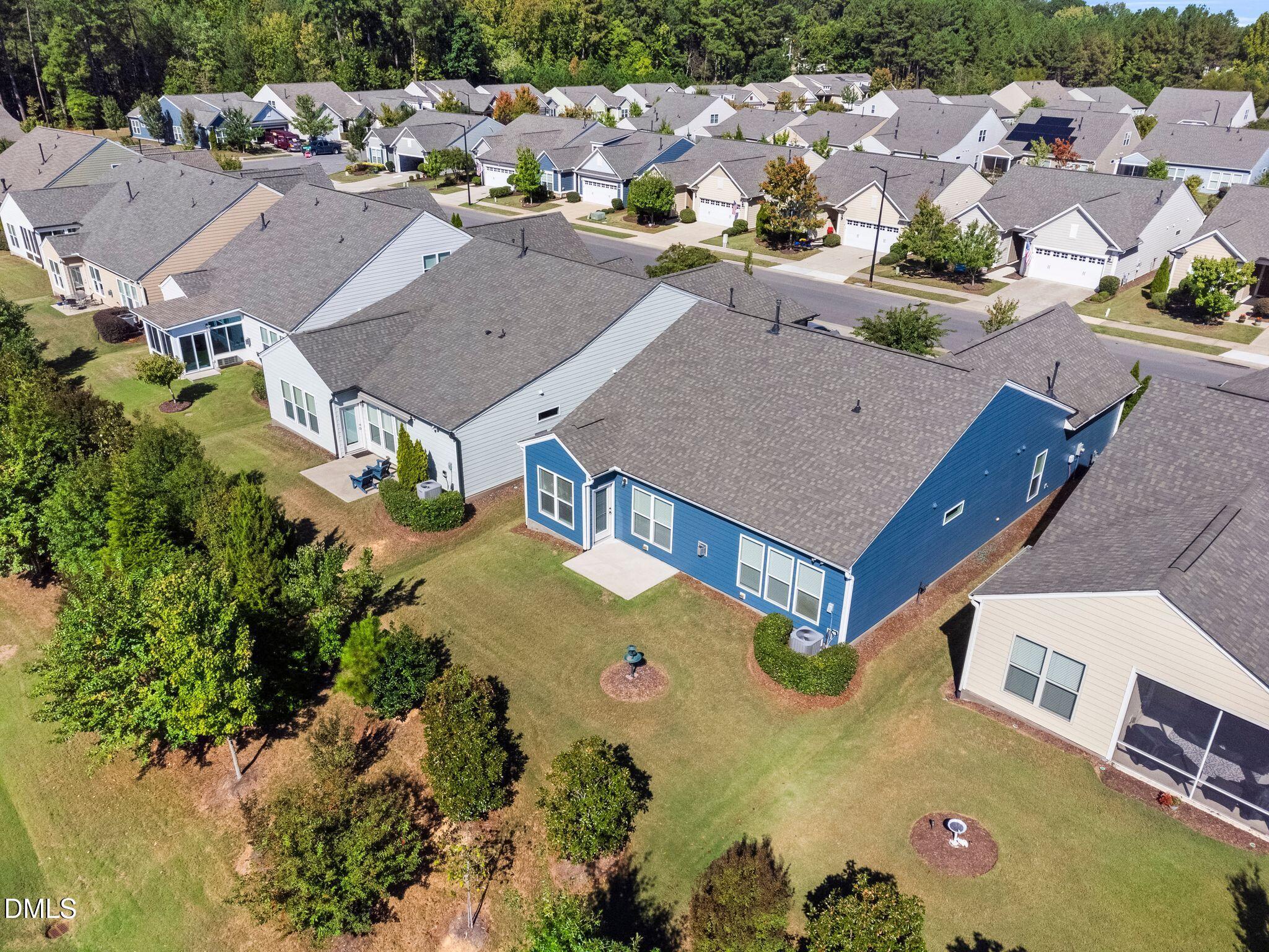 Aerial view of a blue-sided home with a broad roof, landscaped backyard, and neighboring houses.