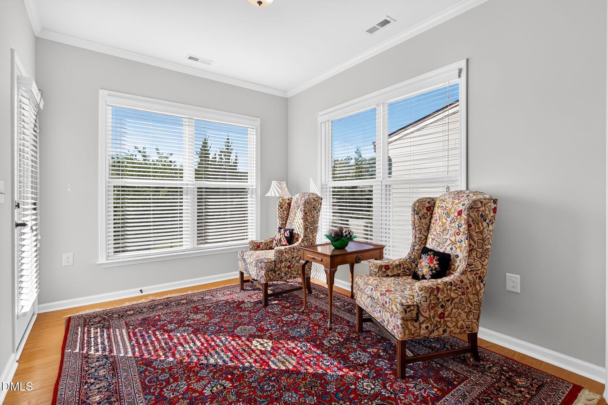 Bright sitting room with floral wingback chairs, large windows, and a red patterned rug.