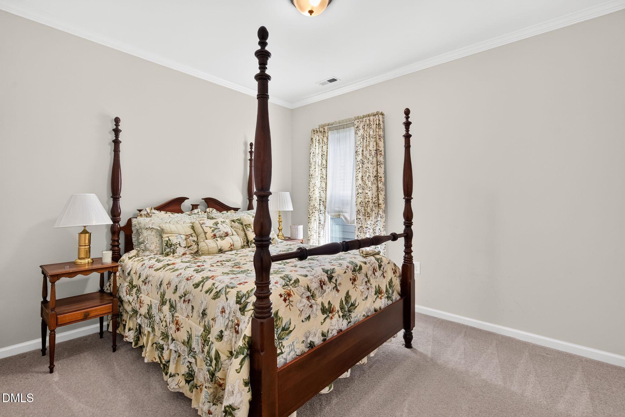 Bedroom with a dark wood four-poster bed and floral bedding beside a curtained window.