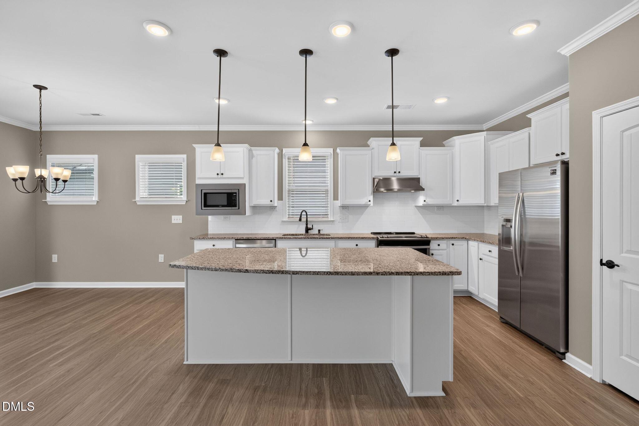 Kitchen with a large granite island, white cabinets, and stainless steel appliances.
