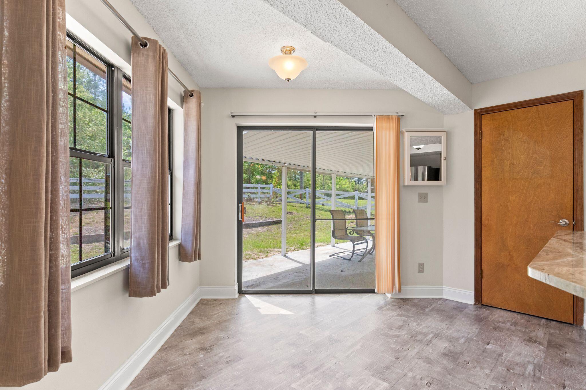 Empty vaulted room with large windows and sliding glass doors to a covered patio.