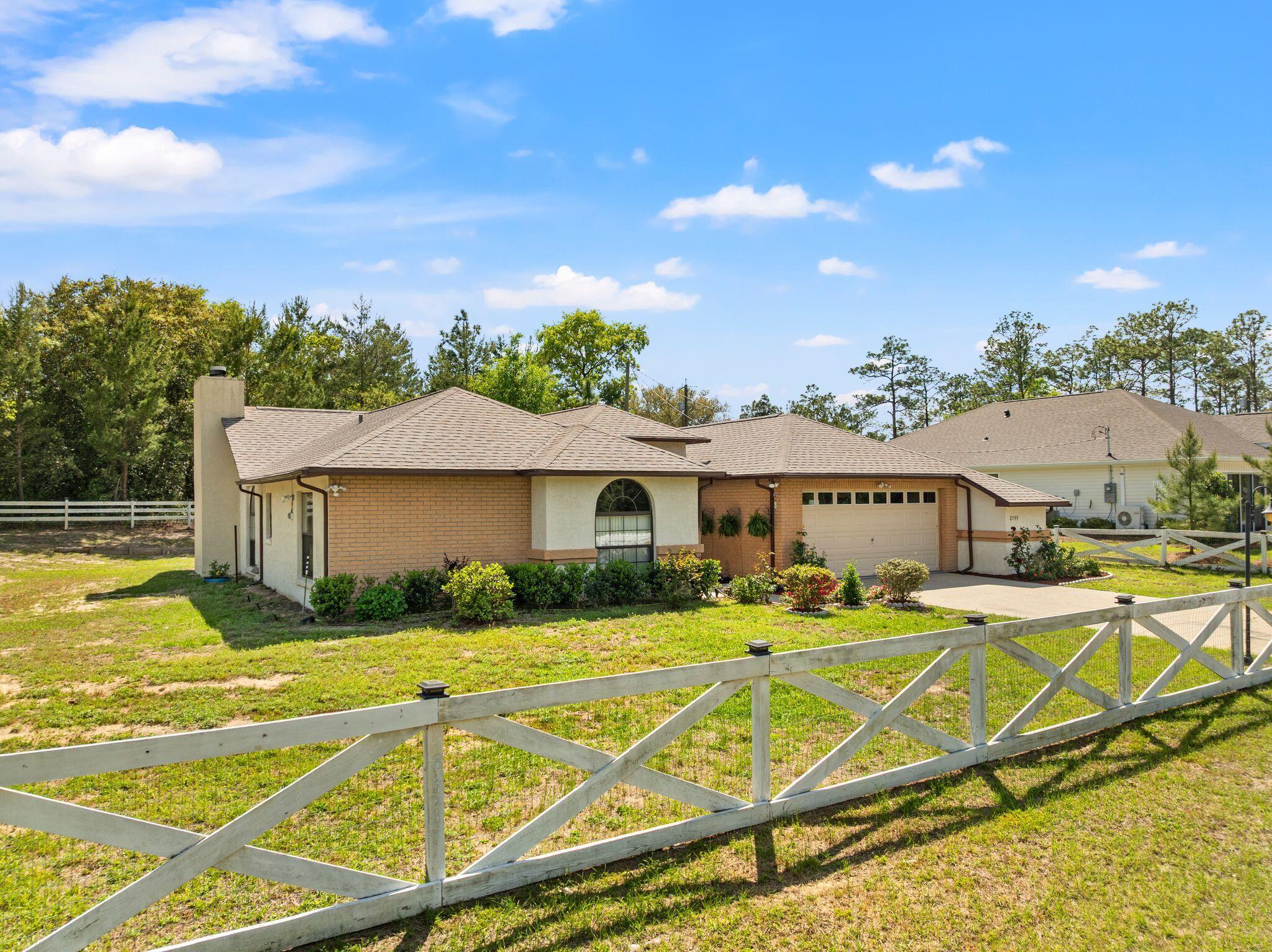 Single-story brick home with an arched window and attached garage behind a white cross-braced fence.
