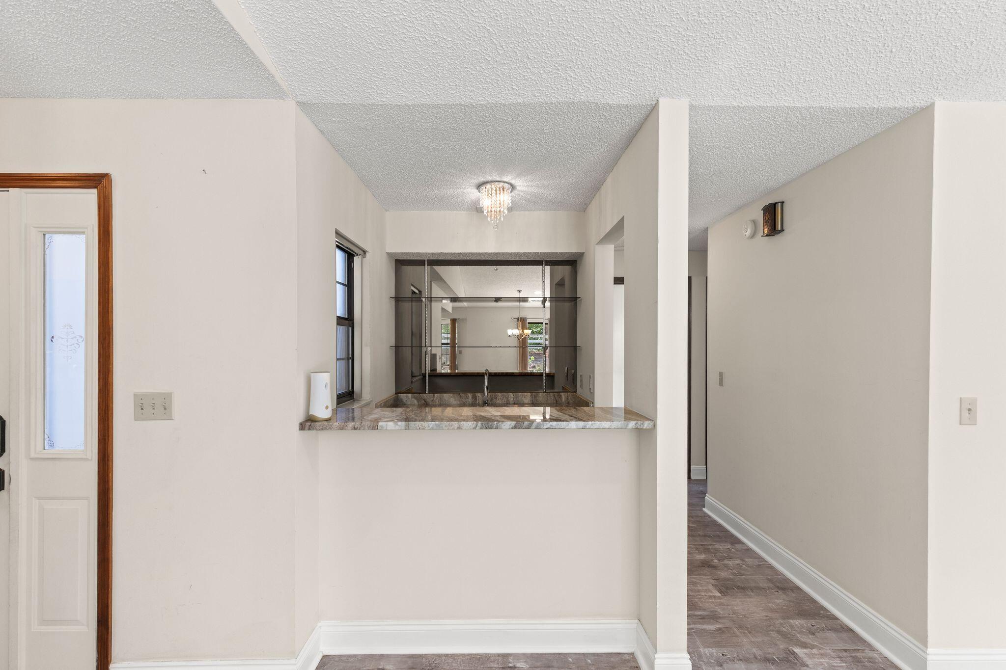 Pass-through counter with mirrored shelving and a chandelier beside a hallway.