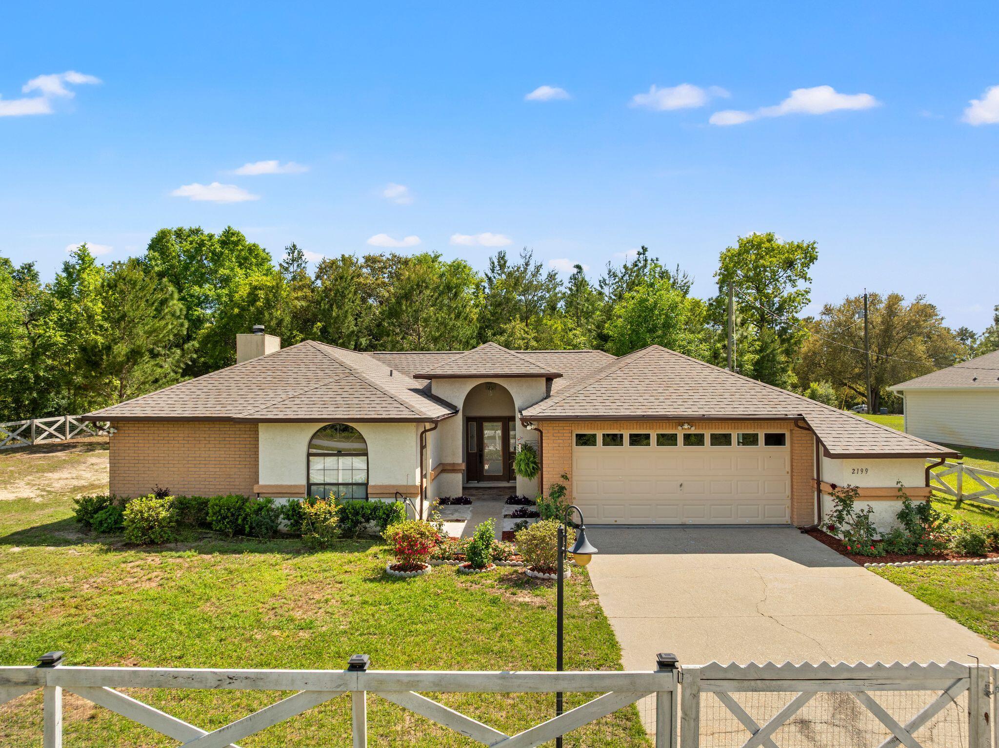 Single-story brick and stucco house with an arched entry, attached garage, and flower beds.