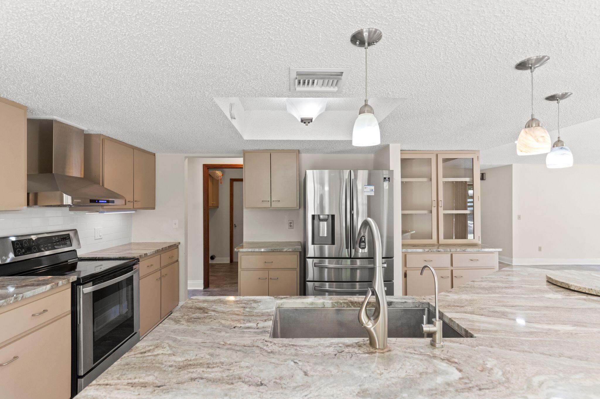 Kitchen with granite countertops, beige cabinets, stainless steel appliances, and a large island sink.