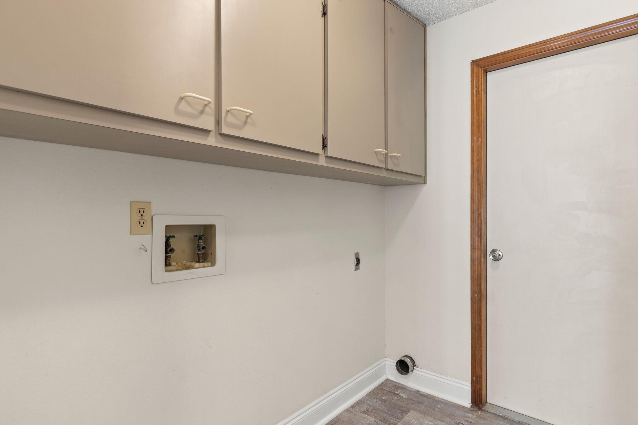 Empty laundry room with upper cabinets, exposed washer hookups, and a dryer vent.