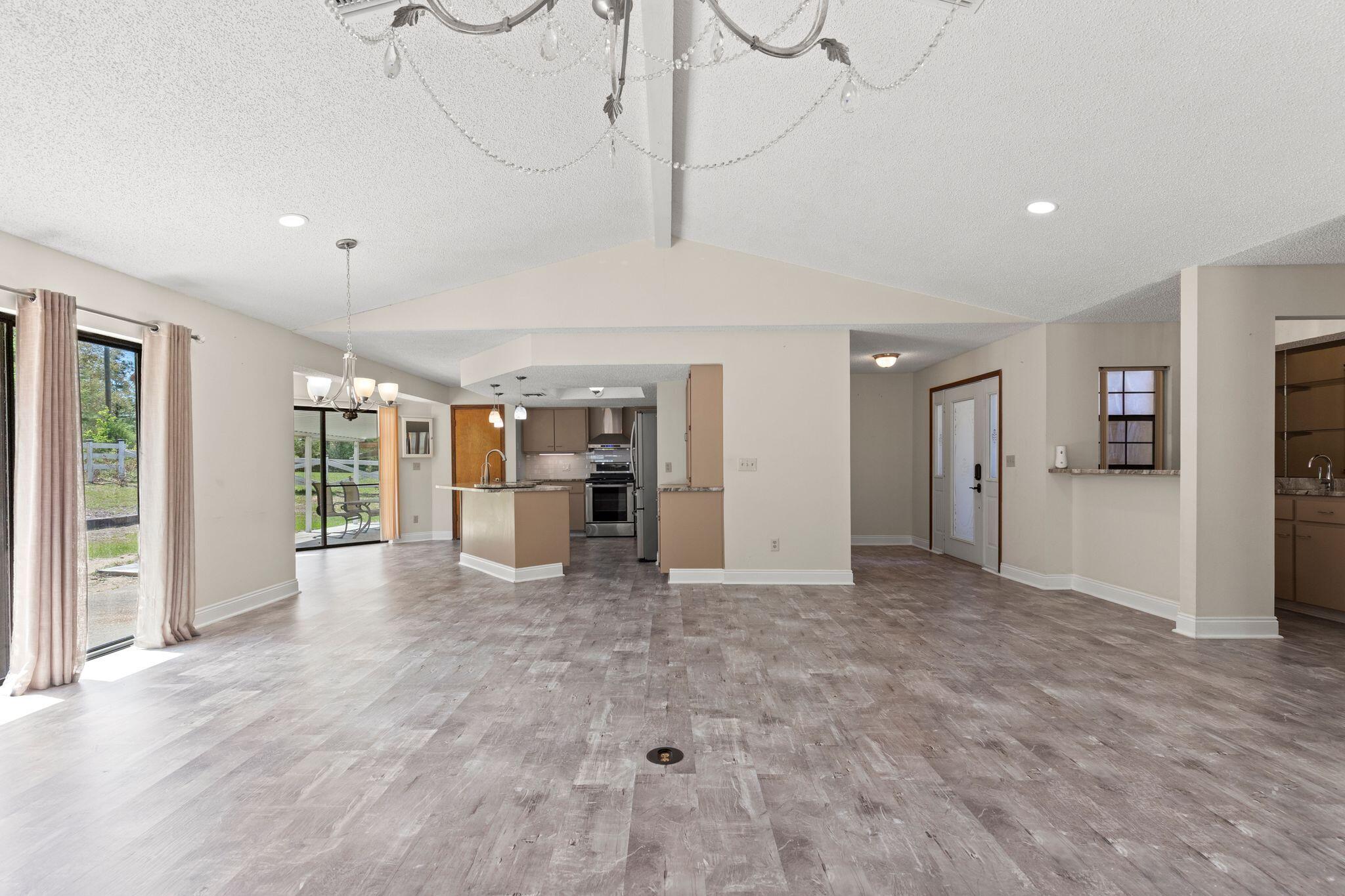 Open-plan living area with vaulted ceiling, wood-look floors, kitchen island, and sliding glass doors.