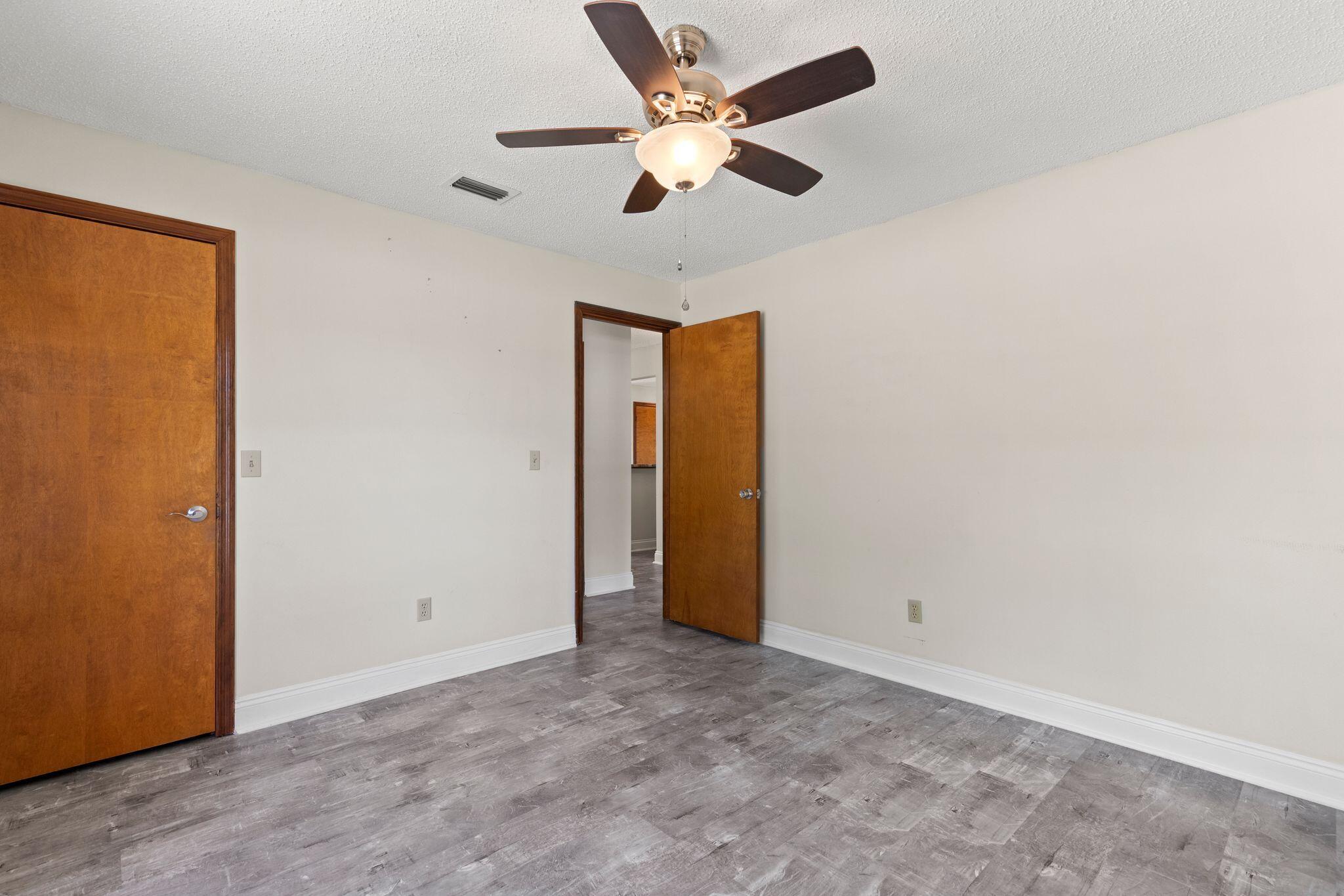 Empty room with gray plank flooring, wooden doors, and a lit ceiling fan.