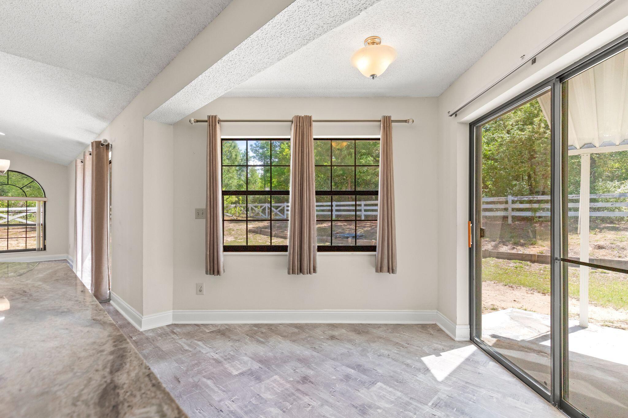 Vacant room with a large curtained window and sliding glass doors to a covered patio.