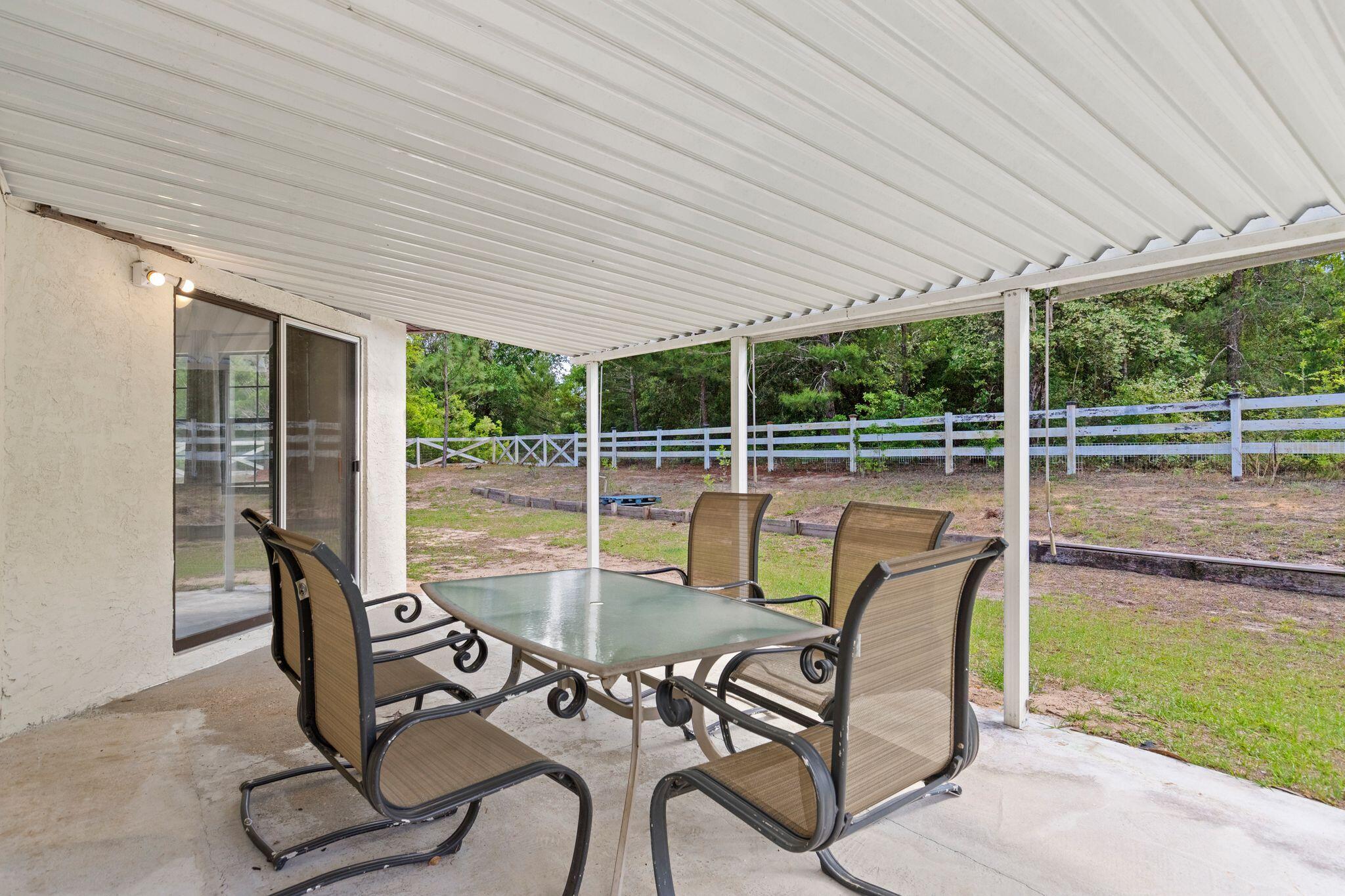 Covered patio with a glass-top dining table and chairs overlooking a fenced yard.