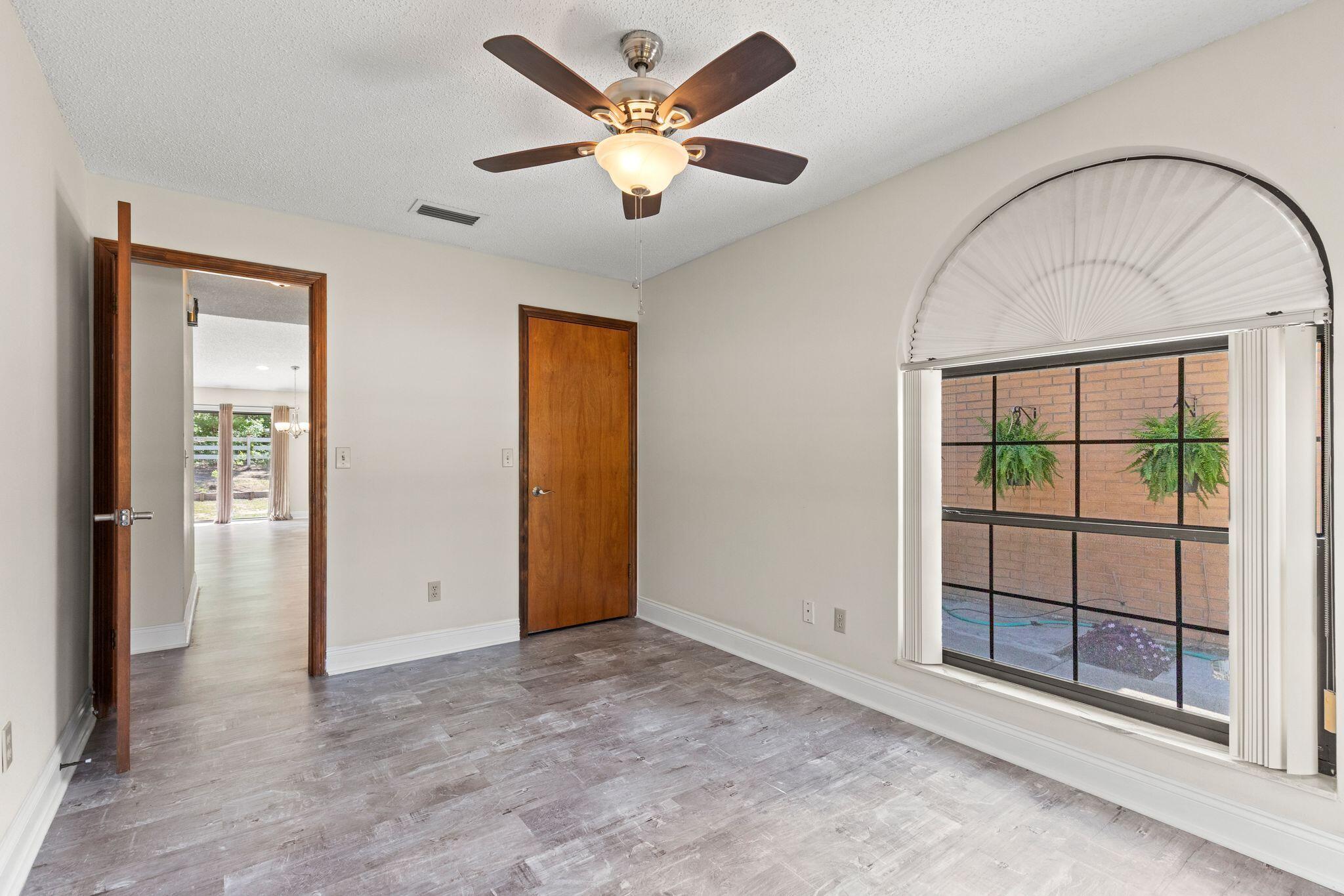 Empty room with gray flooring, a dark wood ceiling fan, and a large arched window.