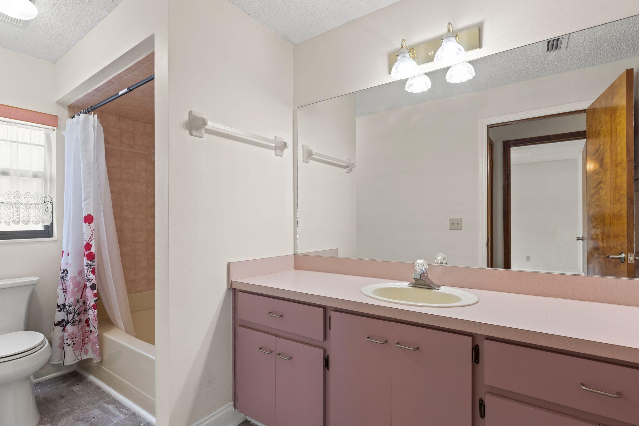 Bathroom with mauve vanity and pink countertop beside a tub with a floral shower curtain.