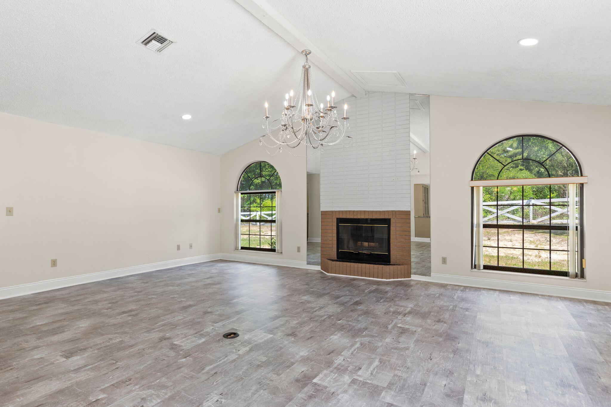 Vacant living room with a brick fireplace, chandelier, and large arched windows.