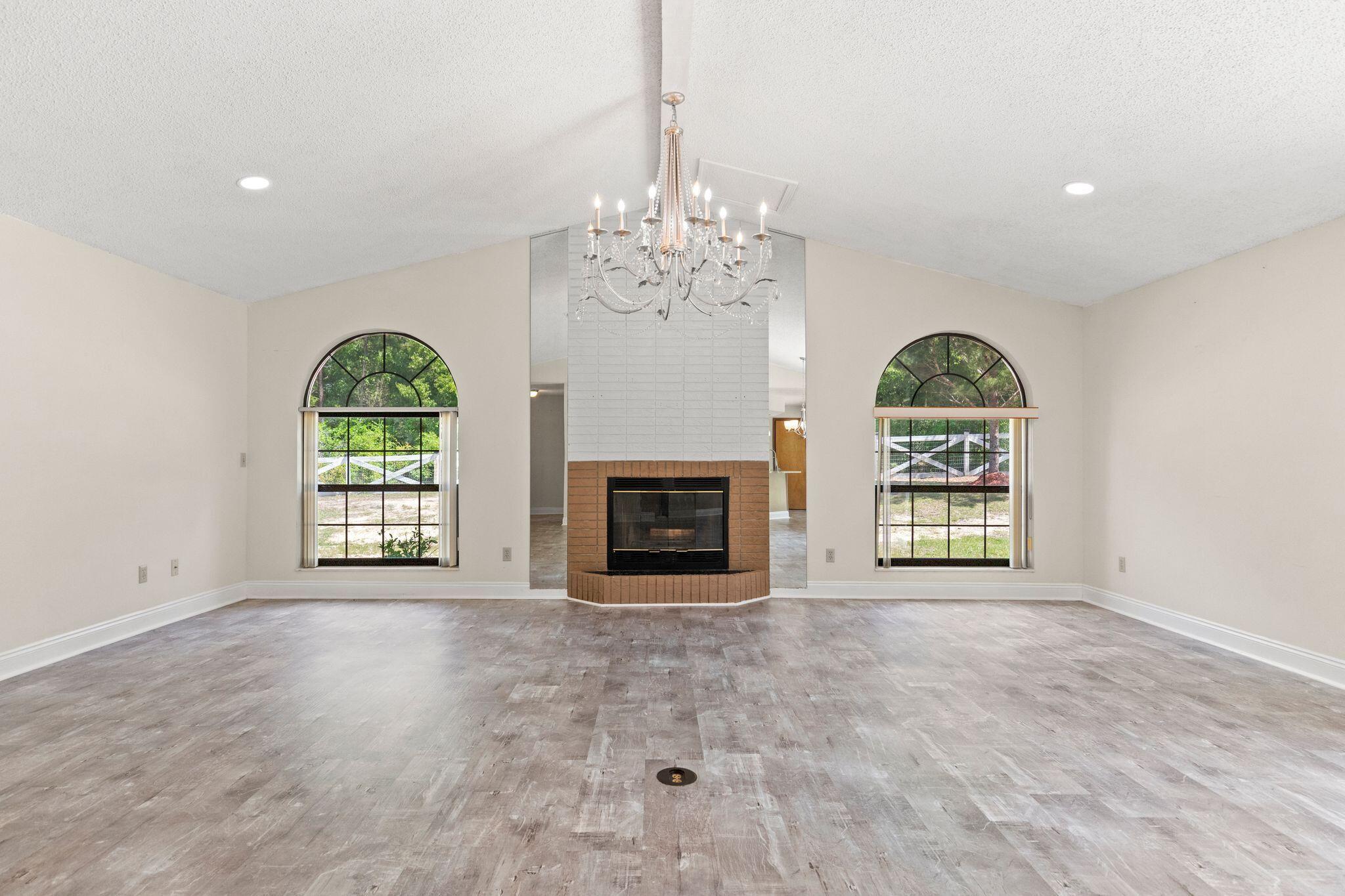 Vacant living room with a brick fireplace, mirrored surround, arched windows, and chandelier.
