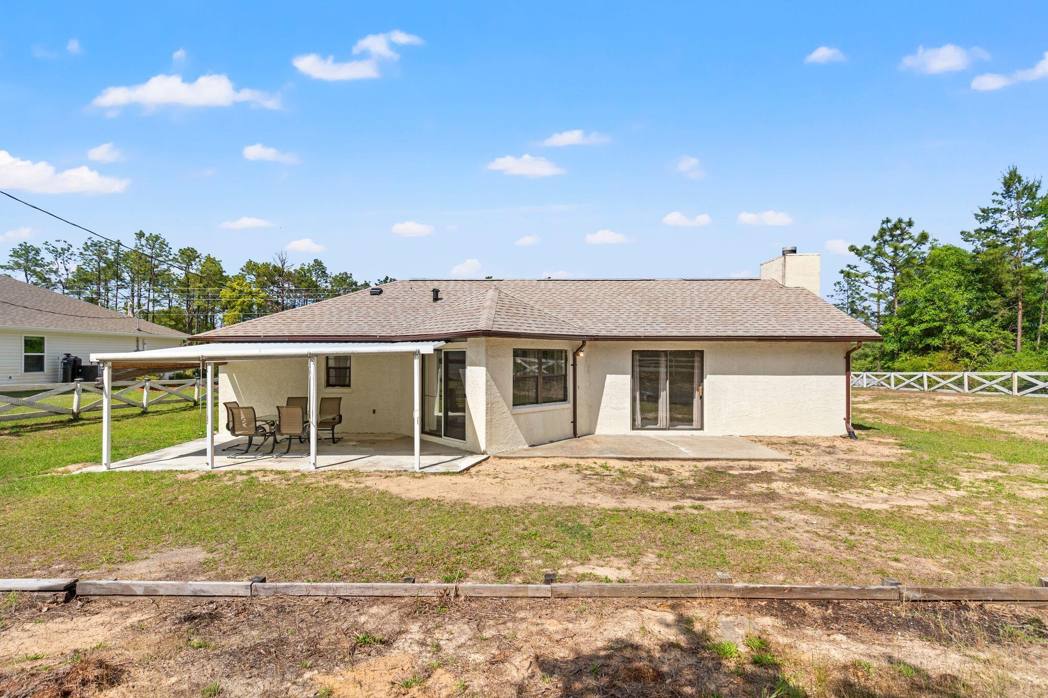 Rear of a single-story home with a covered patio, outdoor seating, and a fenced yard.