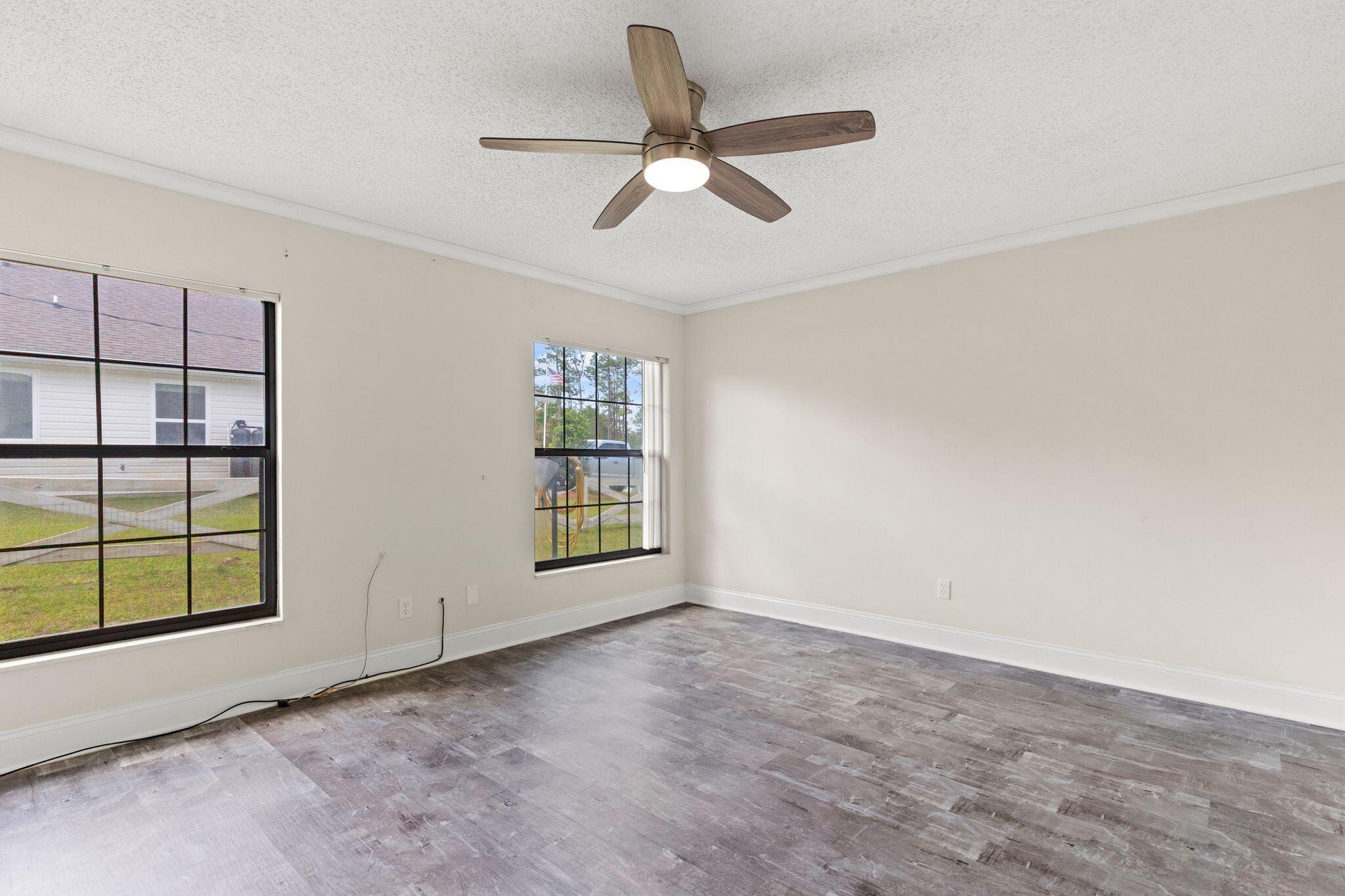 Empty room with plank flooring, two windows, and a wood-blade ceiling fan.