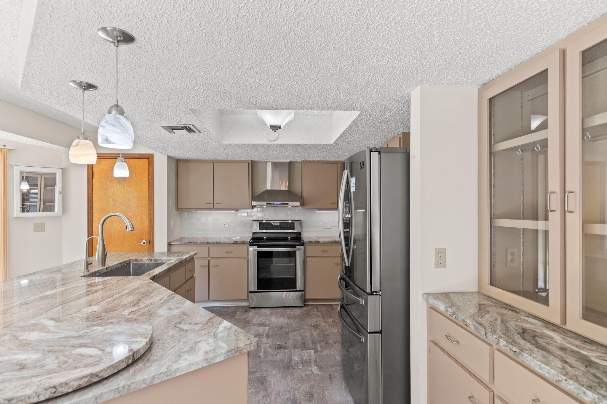 Kitchen with a stone-topped island, taupe cabinets, stainless steel appliances, and glass-front storage.