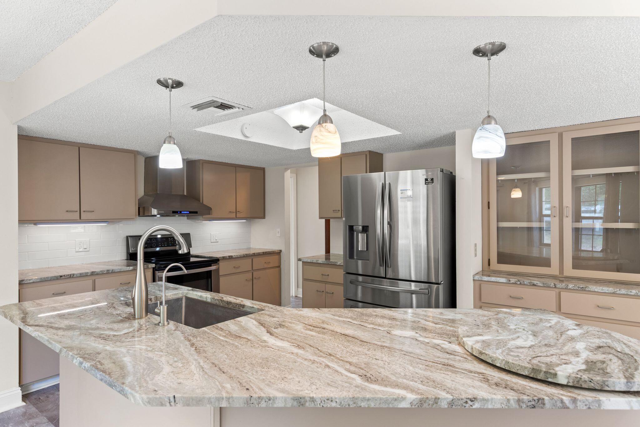 Kitchen with a broad stone peninsula, undermount sink, and stainless steel refrigerator.