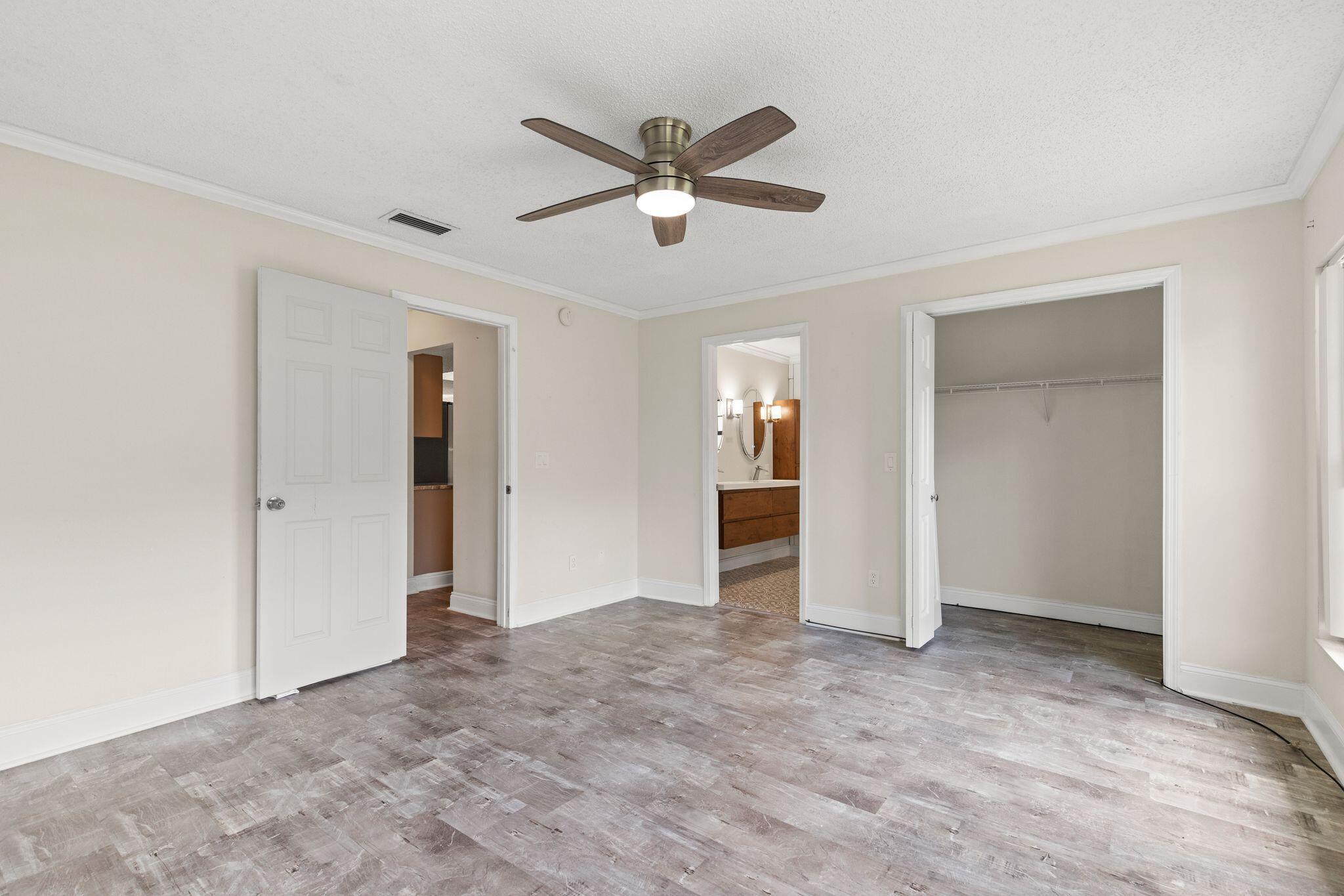 Unfurnished bedroom with a ceiling fan, plank flooring, and open doorways to a bathroom and closet.