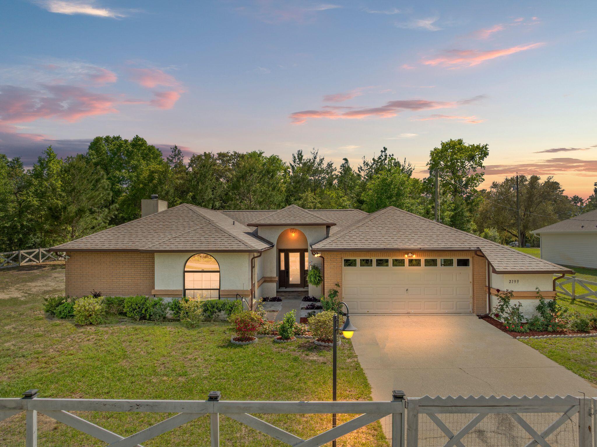 Single-story brick home with an arched entry, two-car garage, and landscaped front yard at dusk.