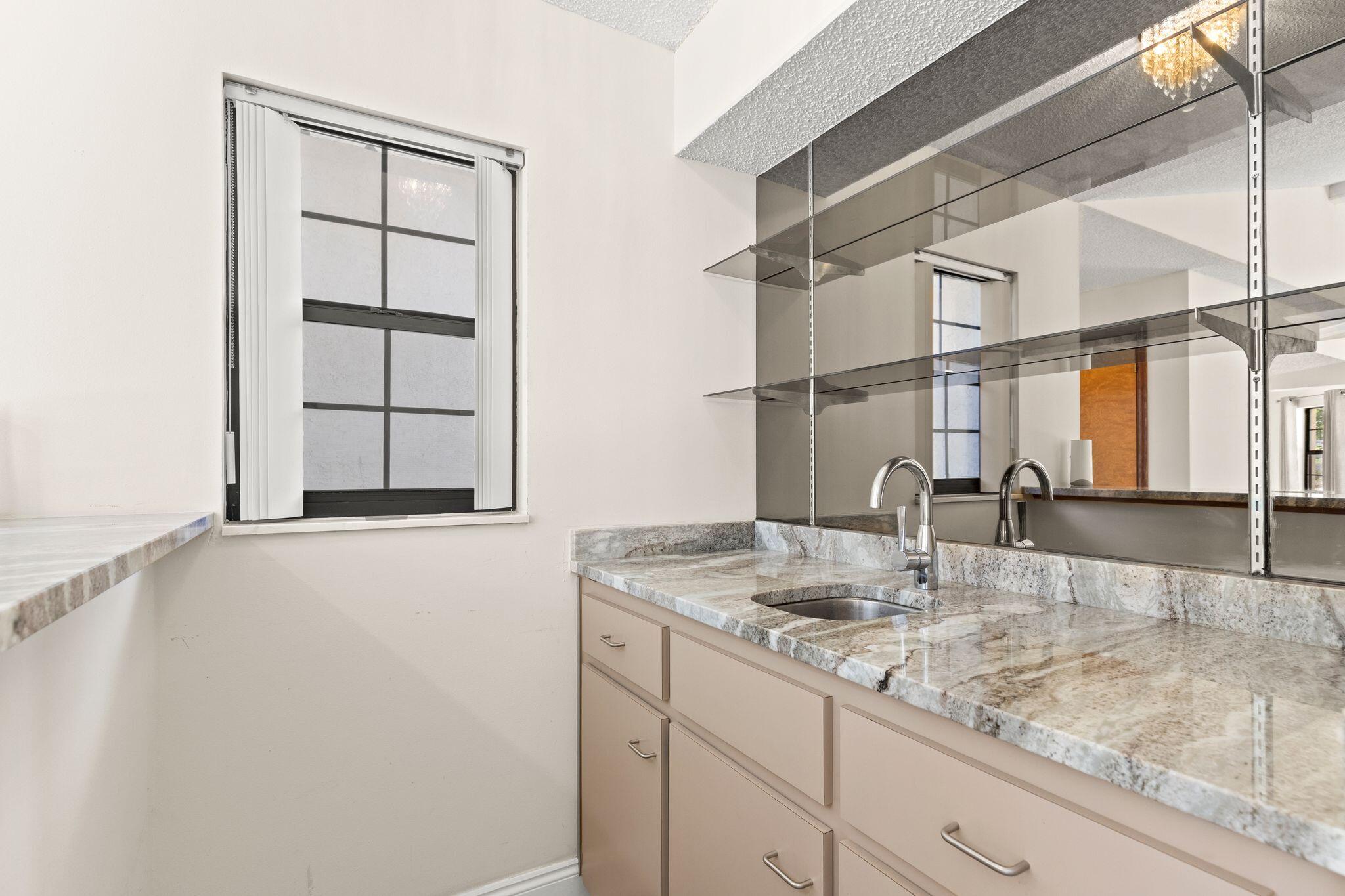 Bathroom vanity with a stone countertop, inset sink, beige cabinetry, and large mirror.