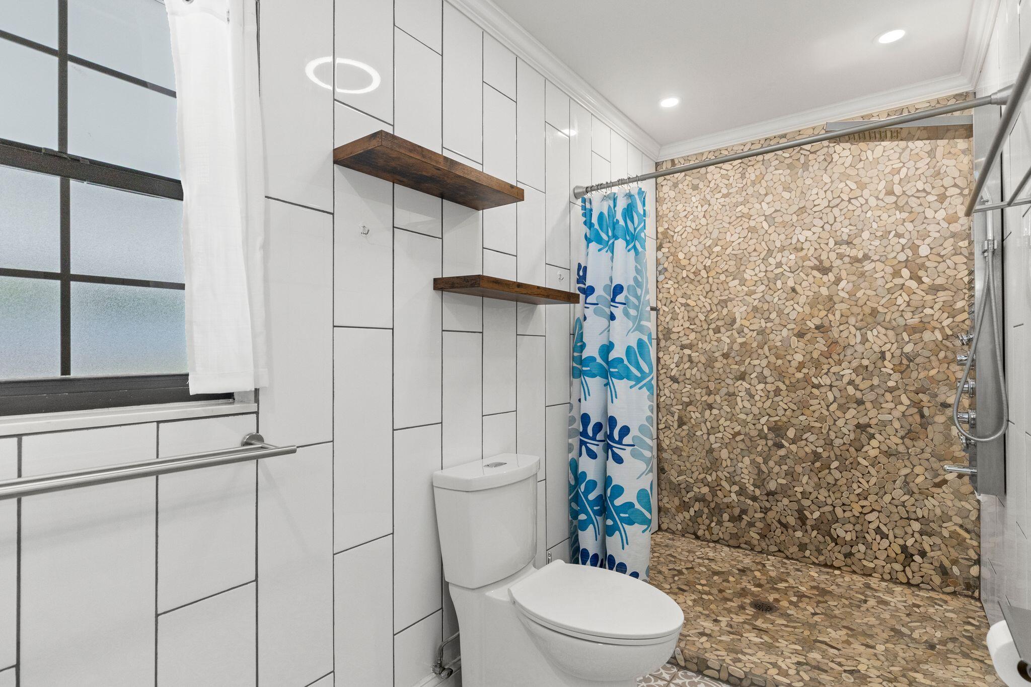 Bathroom with a pebble-tile walk-in shower, blue patterned curtain, and white geometric wall tile.