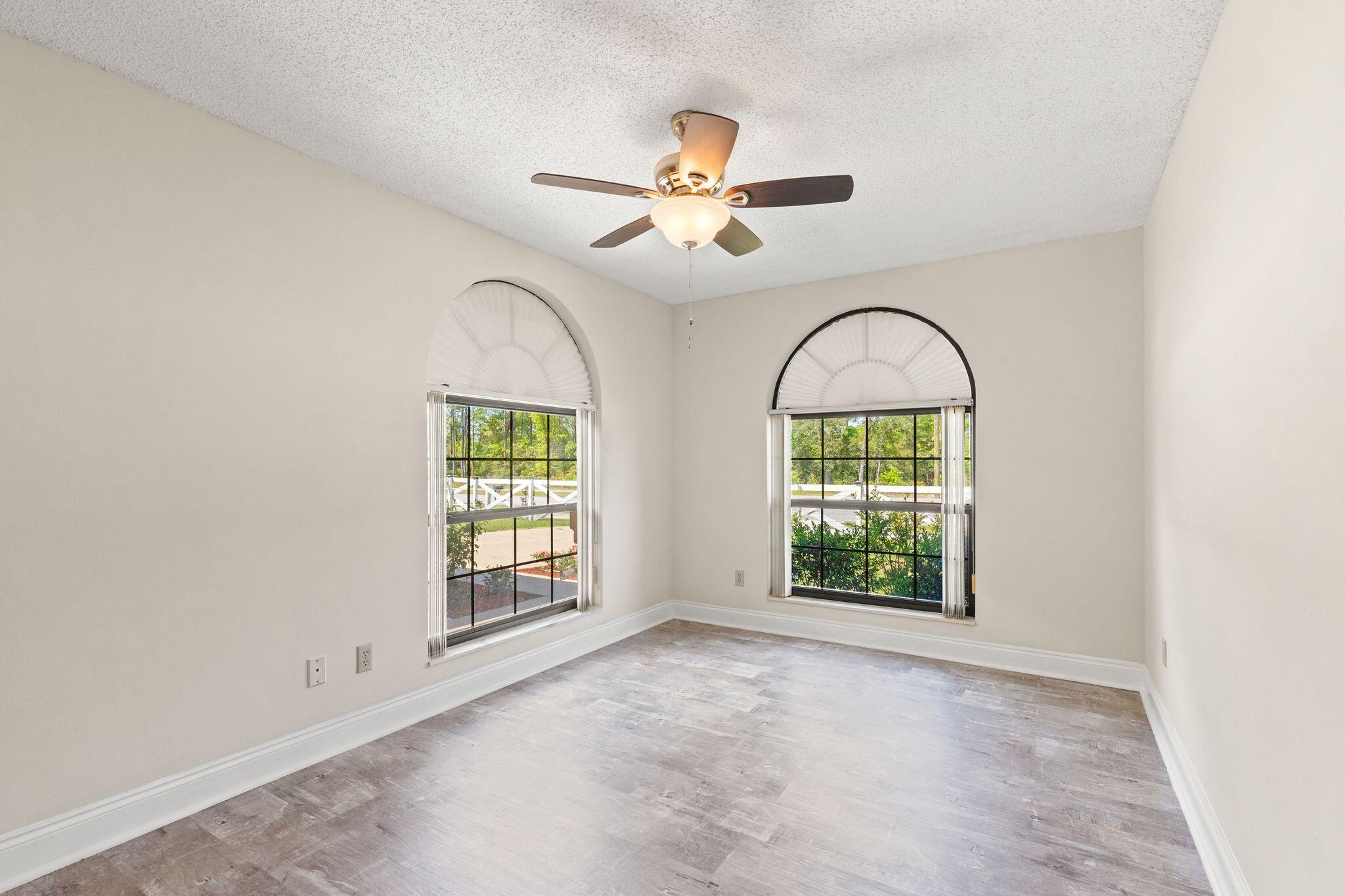 Vacant room with two arched windows, gray-toned flooring, and a ceiling fan.