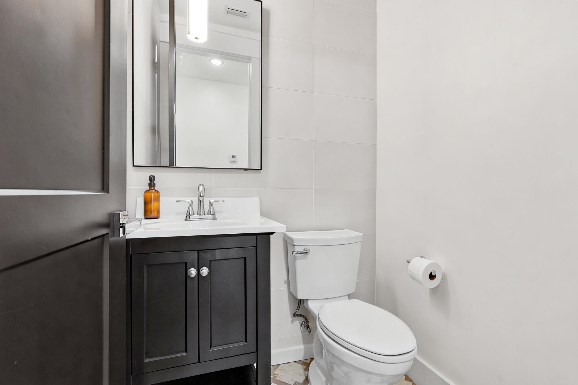Modern bathroom with a dark vanity, white sink, large mirror, and toilet.
