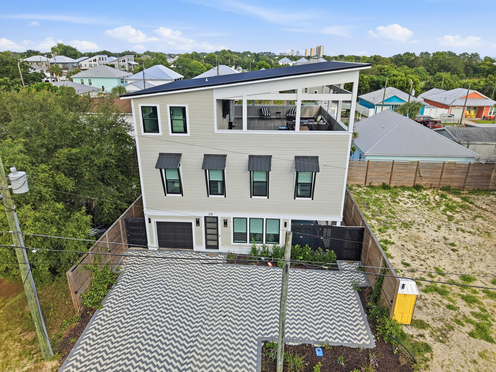 Three-story house with a furnished rooftop terrace and chevron-patterned driveway, seen from above.