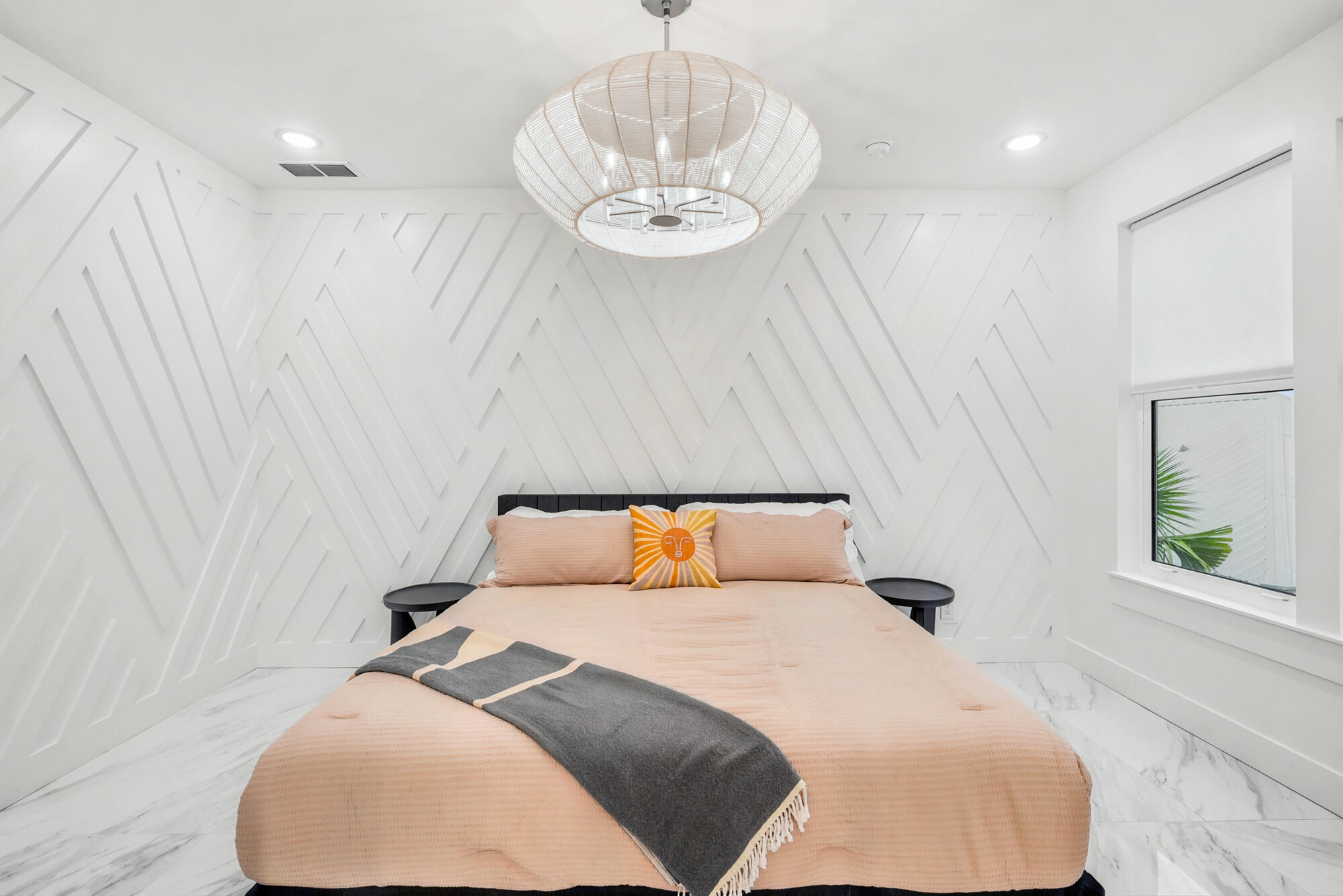 Bedroom with a peach bed, geometric white walls, and a large woven pendant light