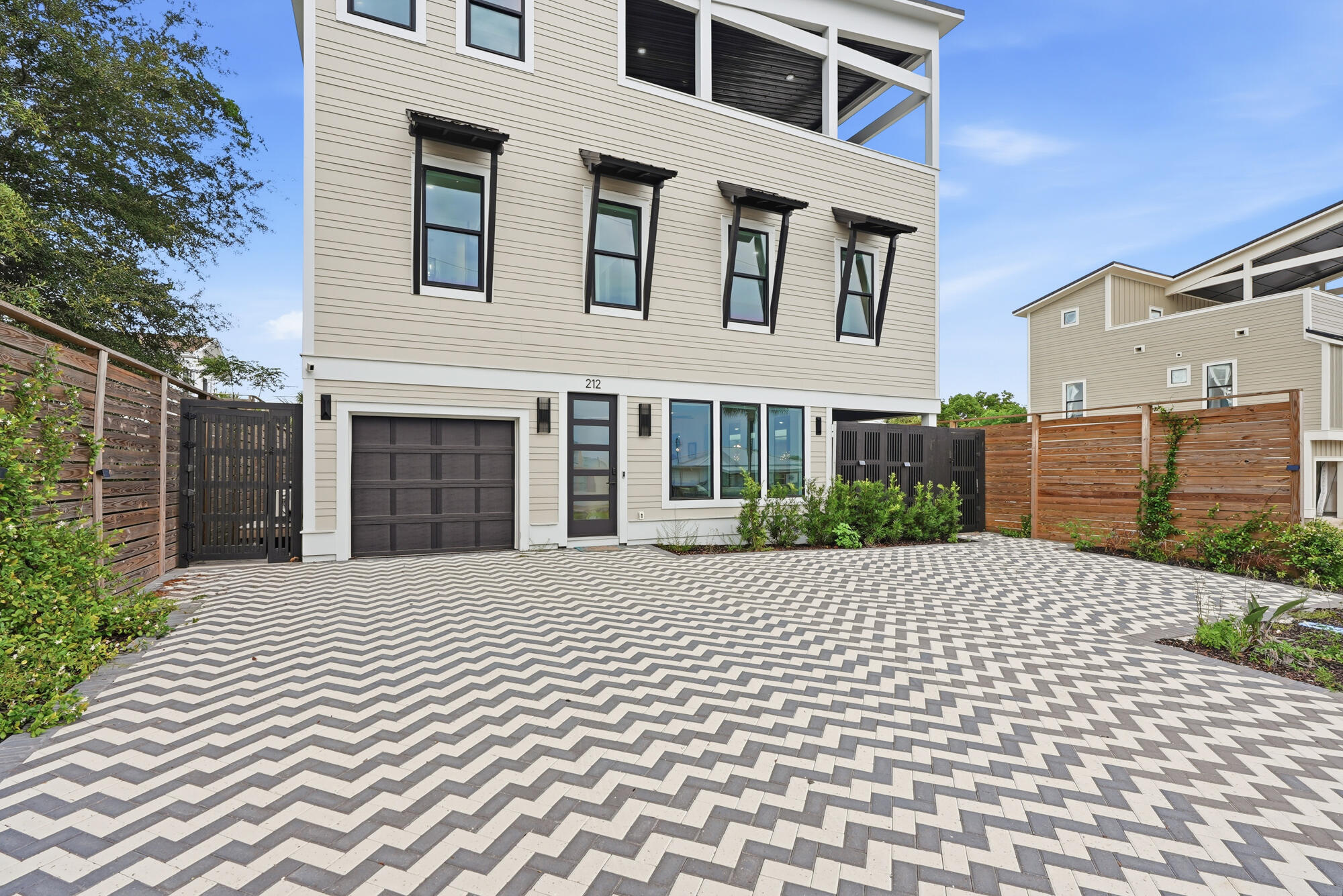 Three-story home with a zigzag paver driveway, garage, covered balcony, and fenced courtyard.