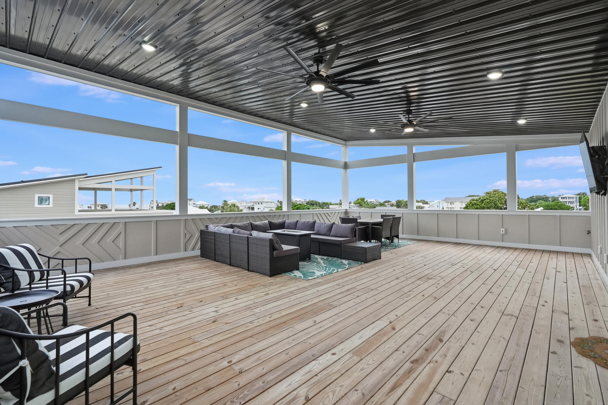 Covered deck with ceiling fans, wood flooring, and furnished seating overlooking nearby homes.