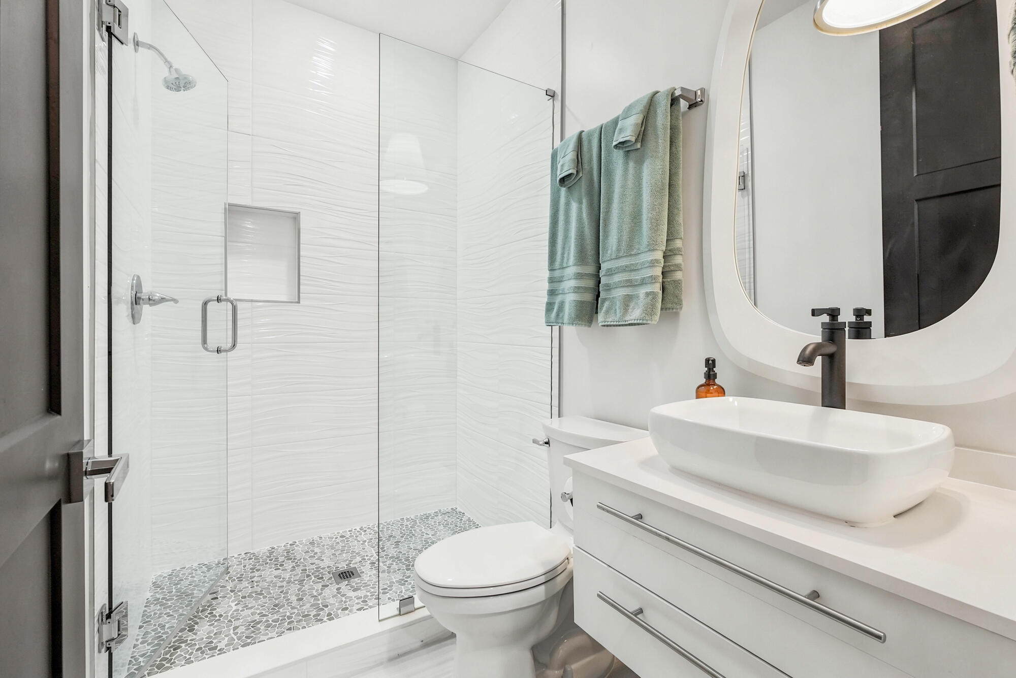 Modern bathroom with a glass walk-in shower, pebble floor, and white vessel sink vanity.