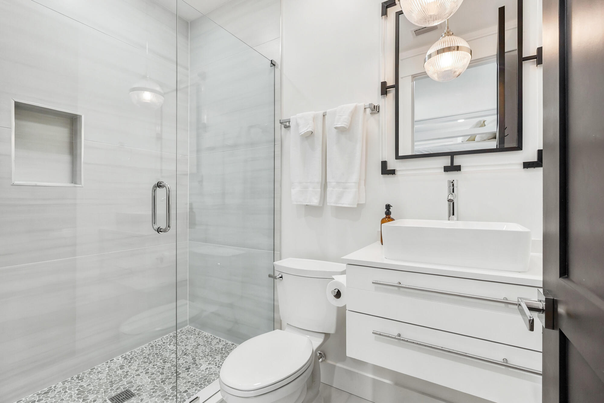 Modern bathroom with glass walk-in shower, pebble tile floor, and white vessel sink.
