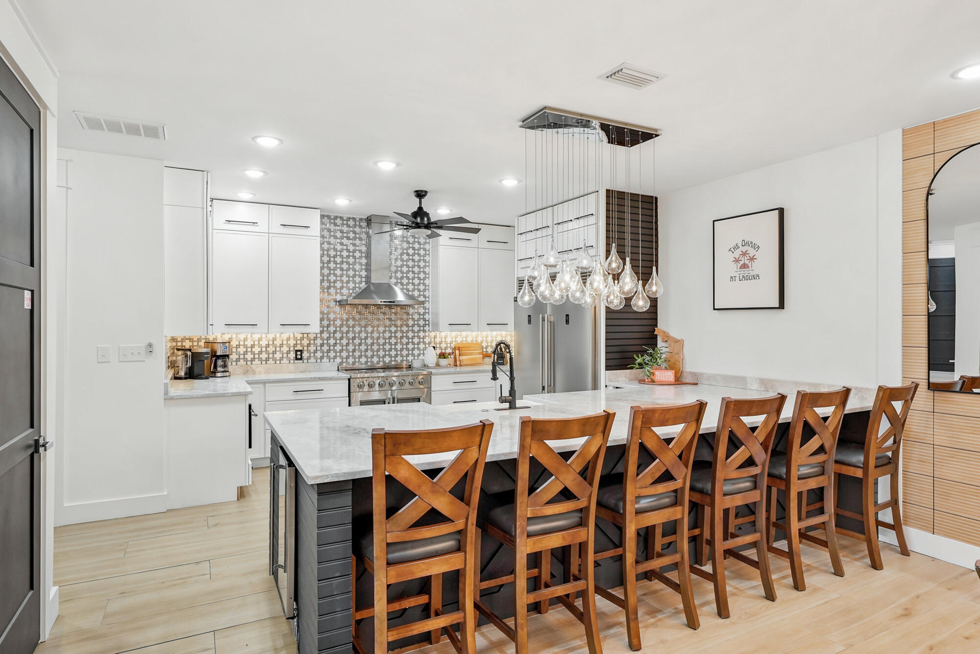 Modern kitchen with a large island, wooden bar stools, patterned backsplash, and glass pendant lights.
