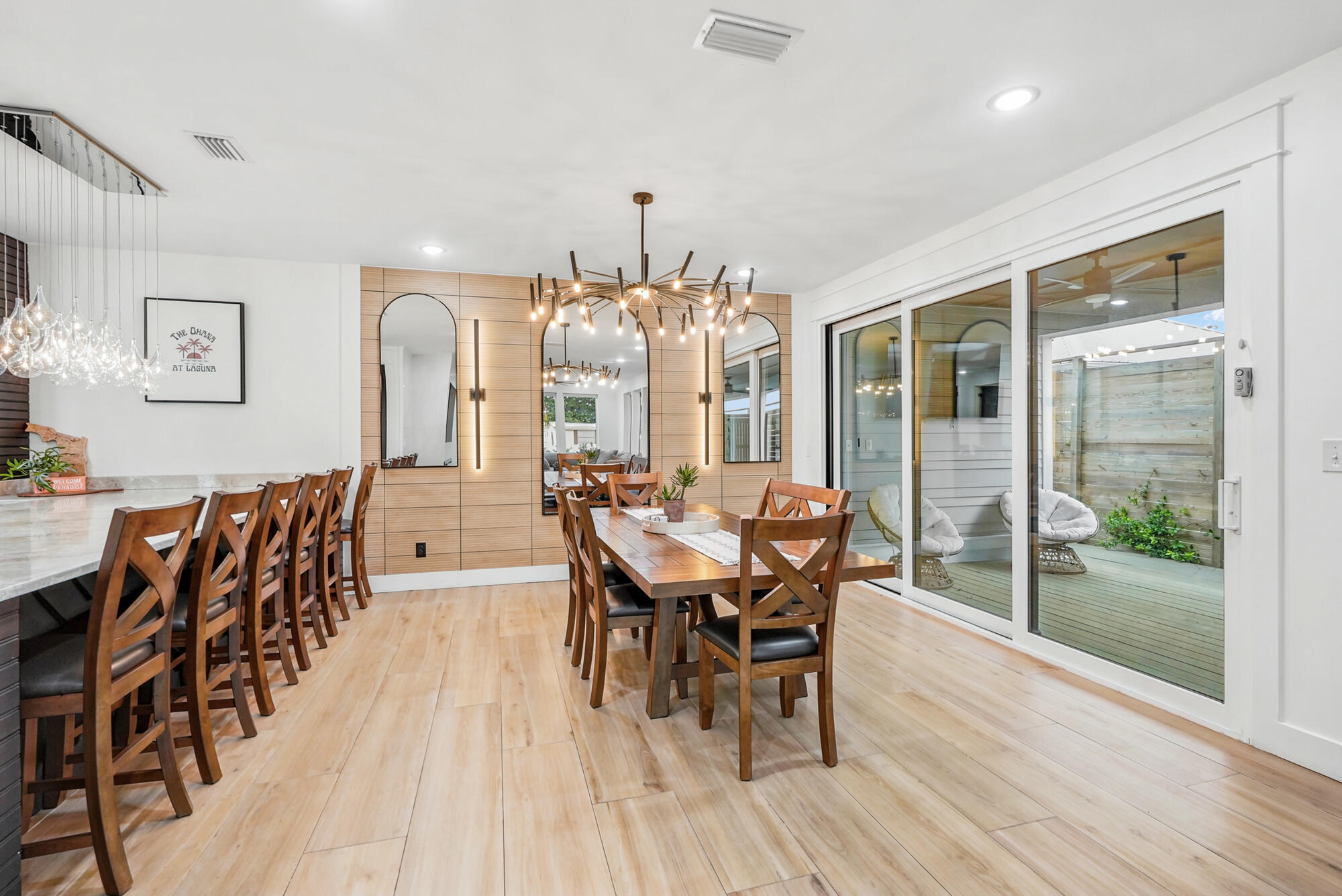 Dining room with a long wooden table, arched mirrors, and sliding doors to a small deck.