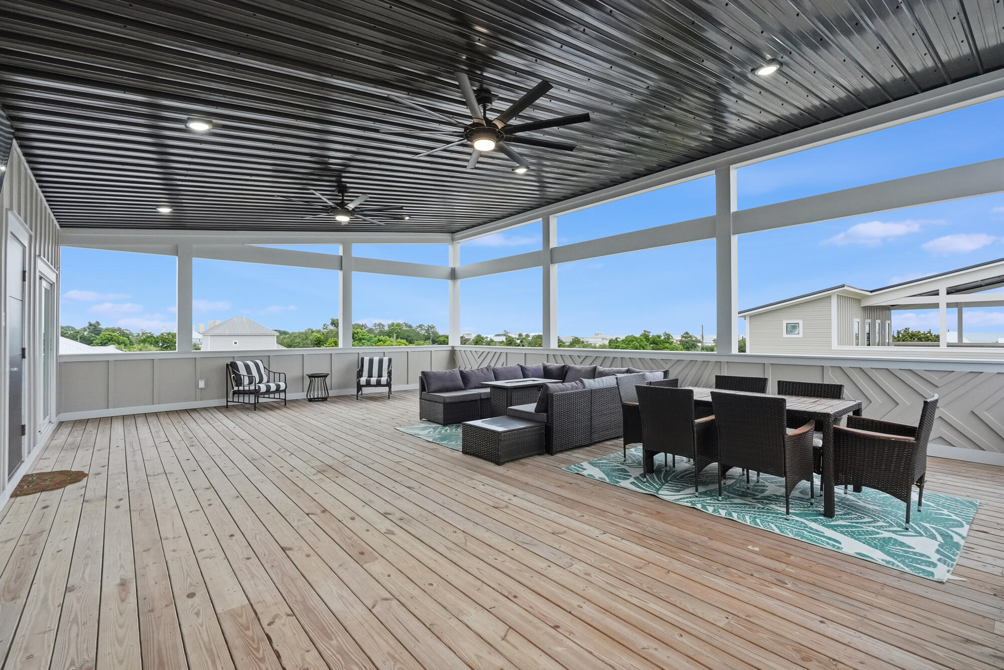 Covered deck with wicker lounge seating, dining set, ceiling fans, and open views of neighboring homes.