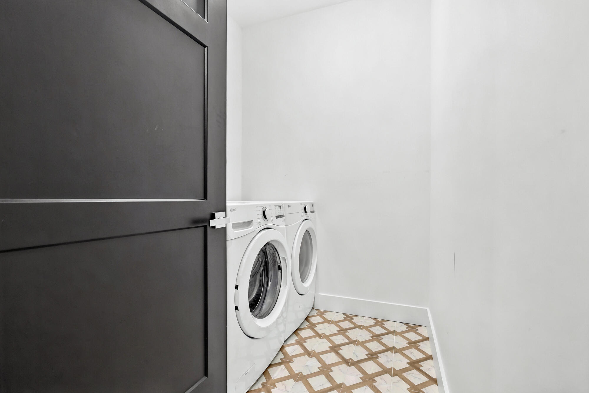 Laundry room with white front-loading washer and dryer and geometric tile flooring.