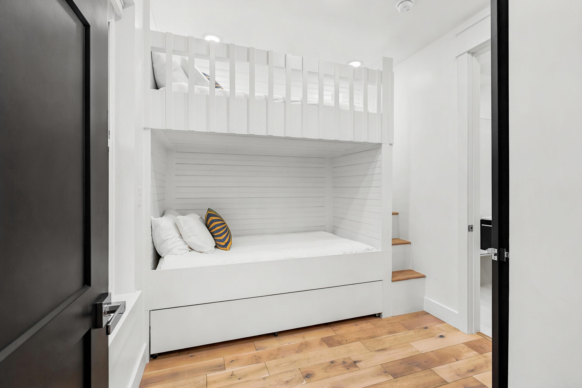 White built-in bunk beds with a mustard-and-navy accent pillow and wooden steps.