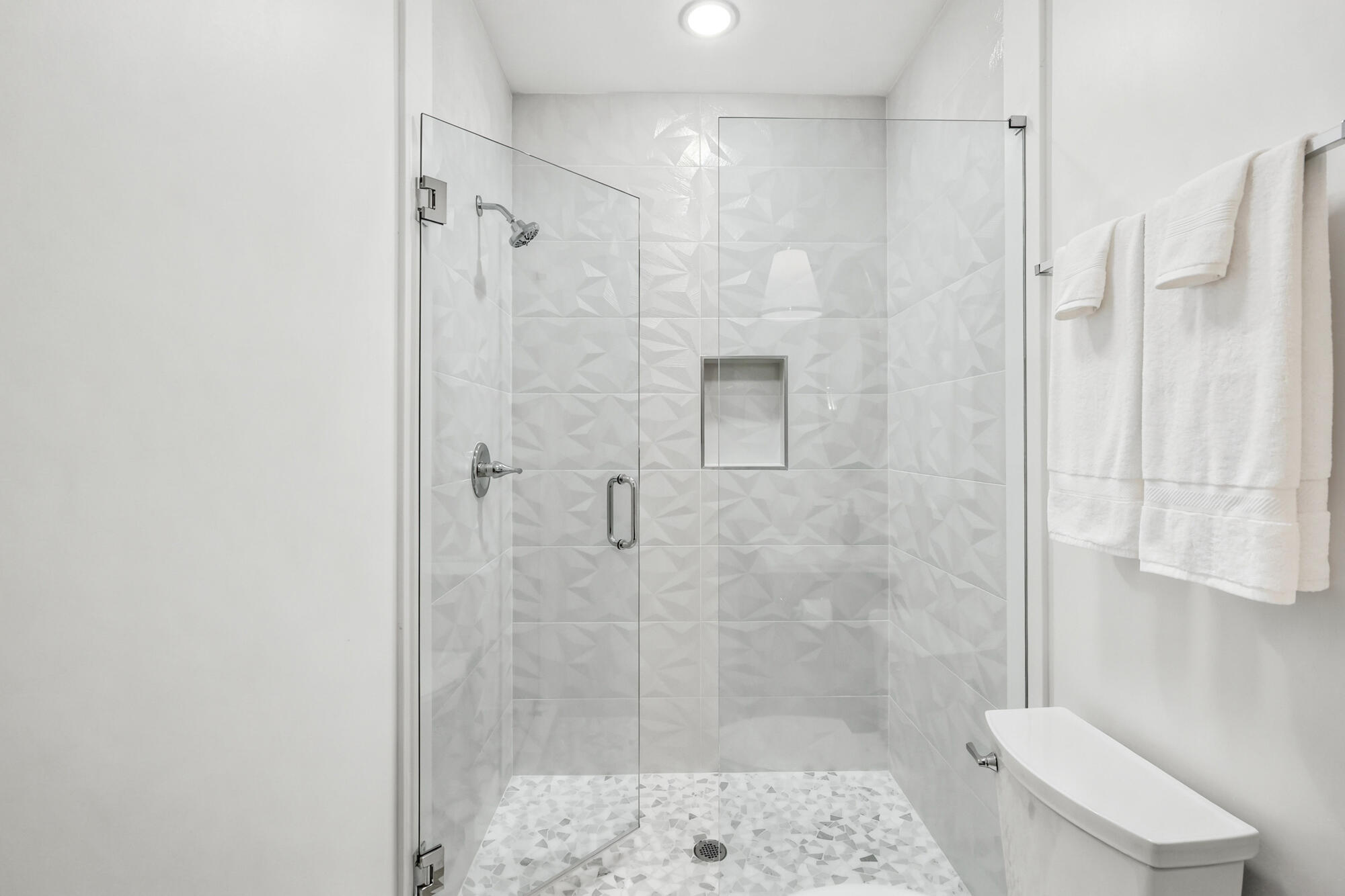 Bathroom with a glass-enclosed shower, geometric gray tile, built-in niche, and mosaic floor.