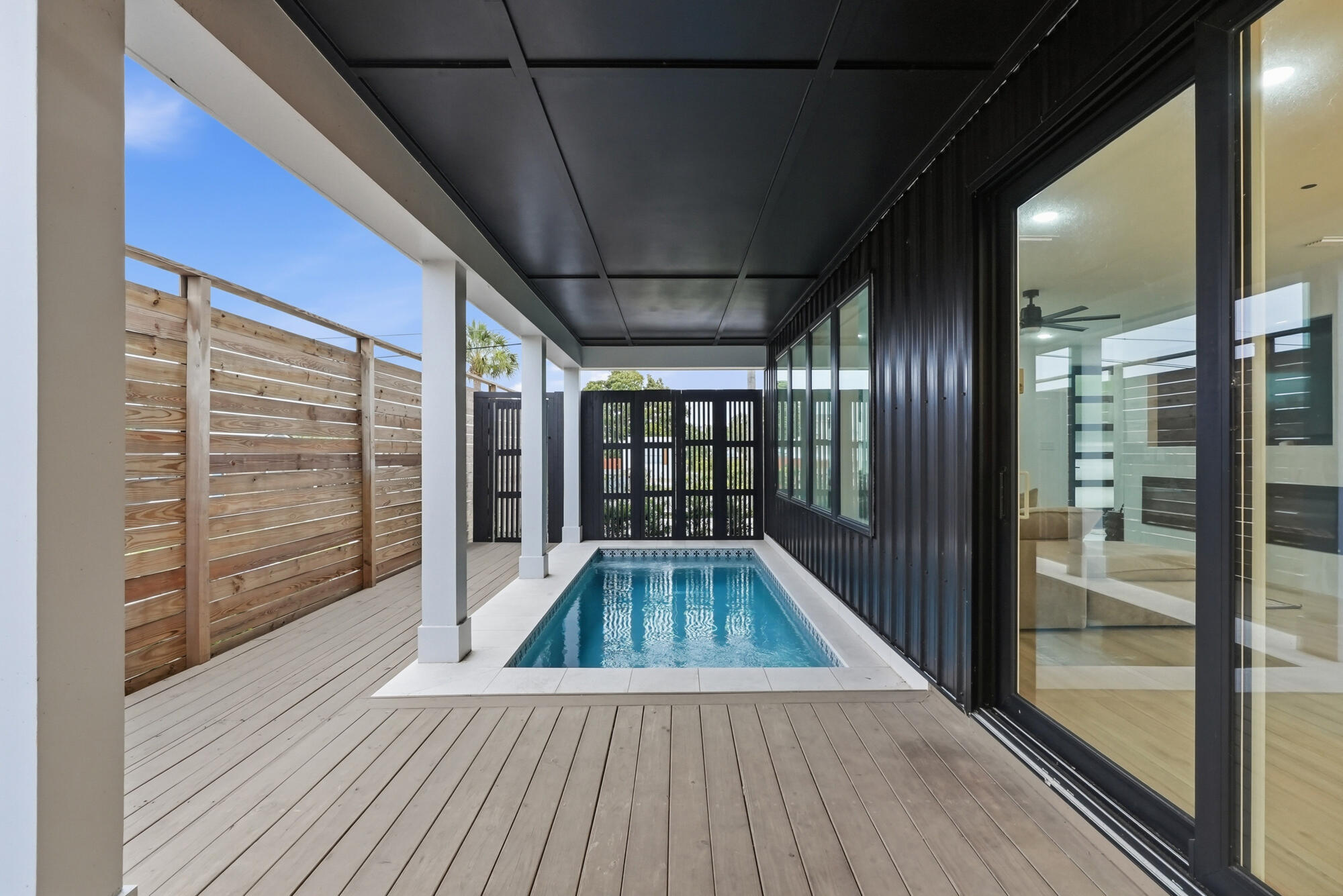 Narrow pool on a covered wood deck beside a modern home, enclosed by a tall privacy fence.