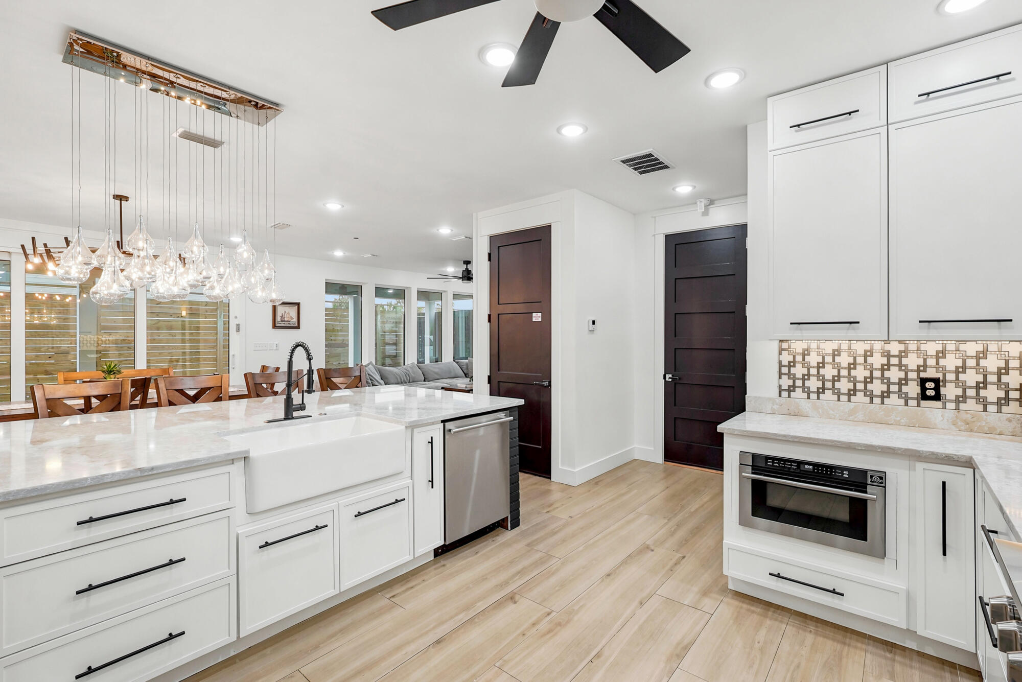 Open-plan kitchen with a large white island, glass pendant chandelier, and patterned tile backsplash.