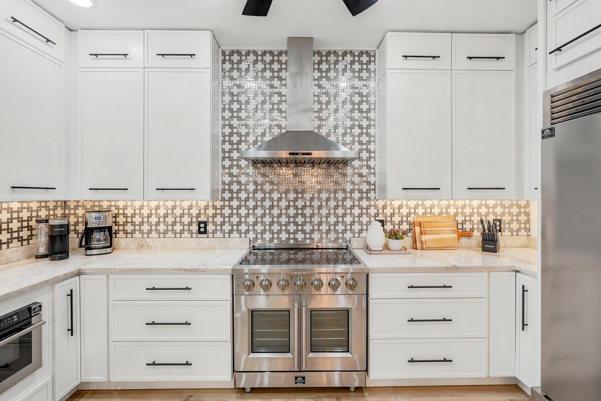 Modern kitchen with white cabinets, geometric backsplash, and stainless steel range.