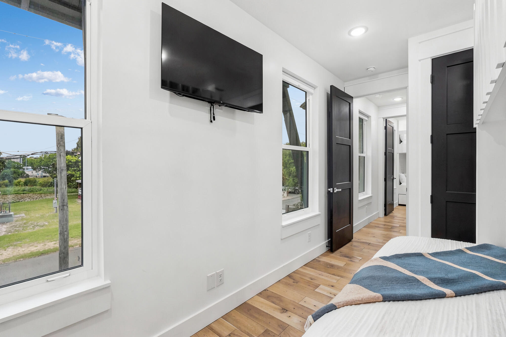 Bright bedroom with a wall-mounted TV, black doors, and large windows overlooking greenery and water.