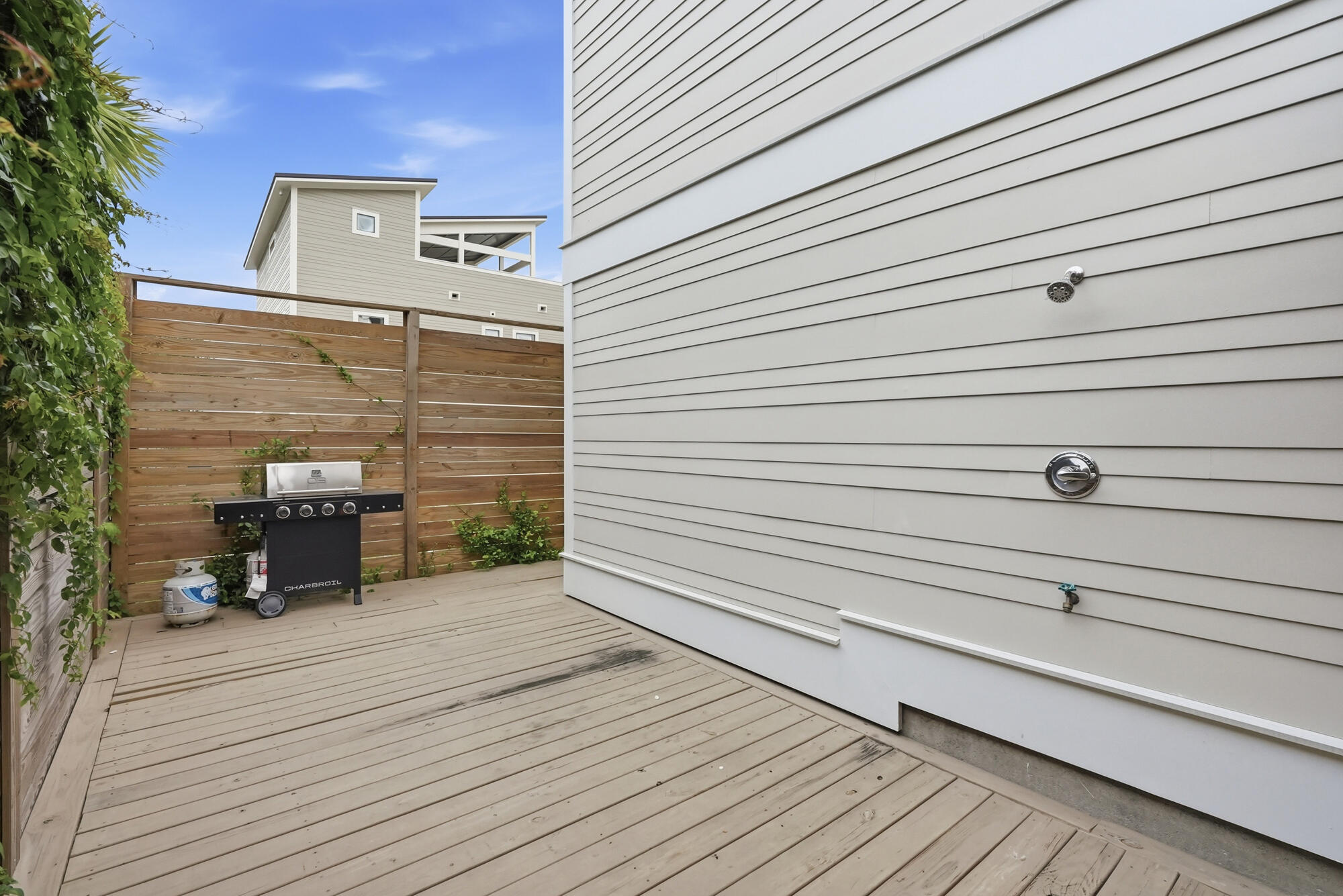 Wooden deck with a grill, privacy fence, and outdoor shower fixtures beside the house.