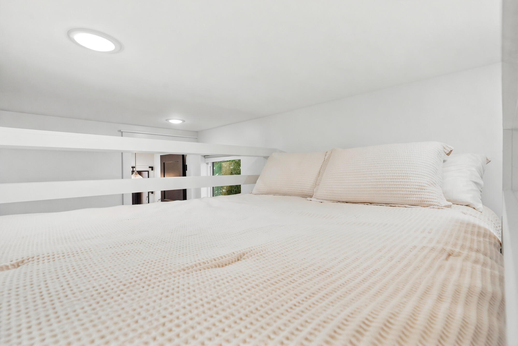 Loft bedroom with a neatly made bed, cream textured bedding, and a low white railing.