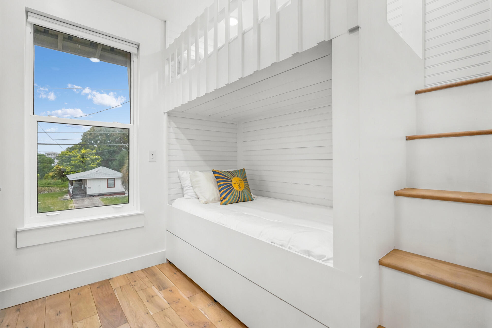 Built-in white window seat with a sun-patterned pillow beside wooden steps to a loft.