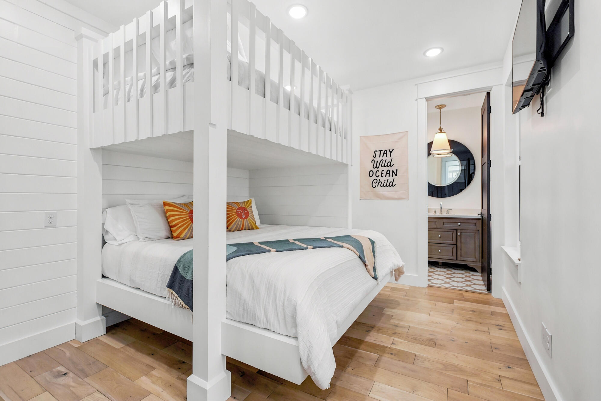 Bedroom with a white built-in loft bed, colorful accent pillows, and a bathroom doorway.